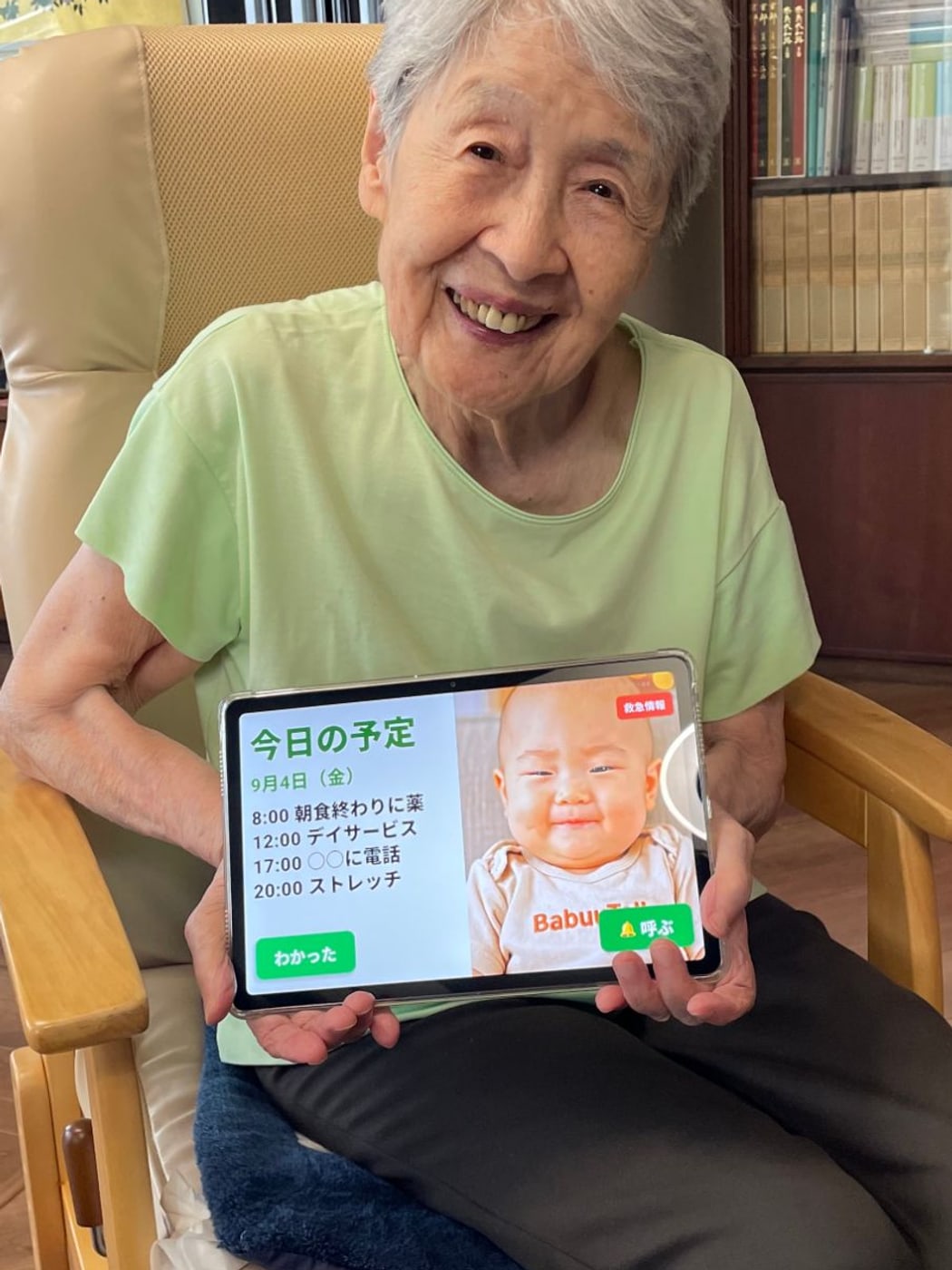 居間の椅子に座り、BabuuTalkの画面を映したタブレットを膝の上に持って笑っているお母様